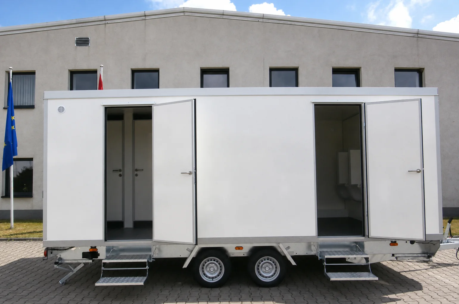 Toilettenanhänger Typ 4+1+4-57 mit geöffneten Sanitärtüren und Tandemachse in Seitenansicht